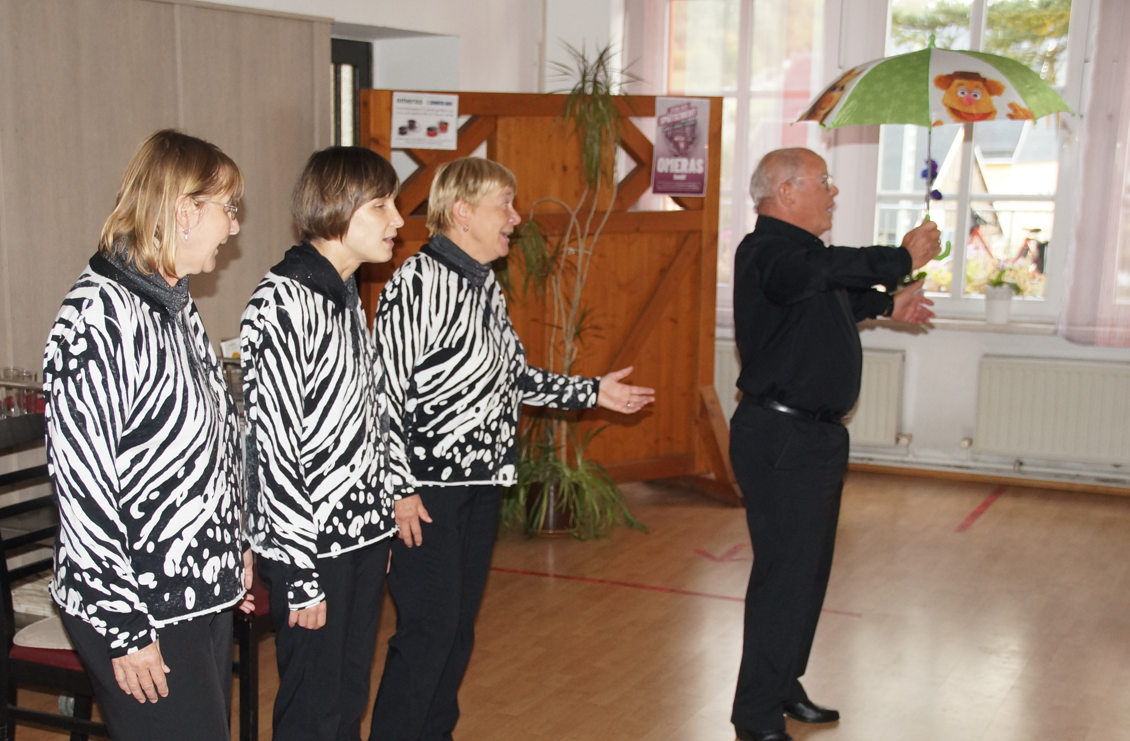 Die Blinden Hühner singen mit ihrem Hahn, der einen Regenschirm in der Hand hält